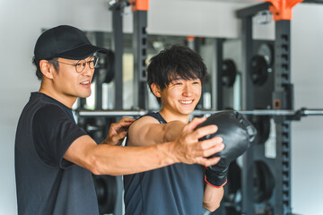 Gym, young Asian man doing boxing exercises at training gym and male trainer staff