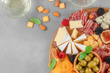 Top view of gourmet charcuterie and cheese board with prosciutto, salami, brie, olives, crackers and berries on gray background with copy space