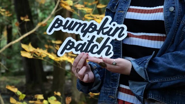 Young Woman holds words Pumpkin Patch in the forest in the Fall with Yellow Tree Leaves 4K Video Stock Footage