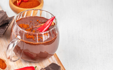 Spicy hot chocolate with chili pepper in glass cup on light background with copy space, creative winter drink concept