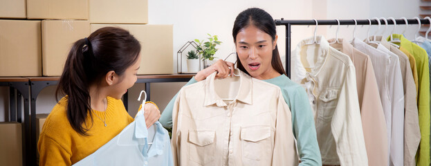 Two young asian woman live online clothing store while showing clothing with tablet on social at home, entrepreneur streaming for selling online clothing and presenting, online seller.