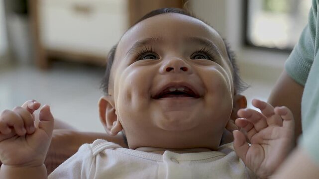 Close up of a happy infant boy with dimples laughing and looking up at an adult, showing pure joy and playful interaction.