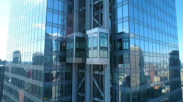 Glass Exterior Elevators Ascending on Modern High Rise Building with Surrounding Cityscape Reflected in Facade