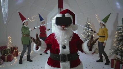 Santa Claus wearing virtual reality headset while children in elf costumes play with light sabers around Christmas trees in an igloo. - Powered by Adobe