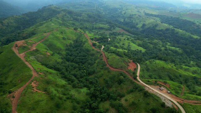 A tilt-down aerial of winding red dirt roads cutting through misty forest hills in Quinawan in Bataan, Philippines