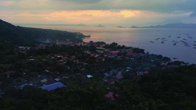 A forward aerial of Talisay town glowing under sunset light across the calm expanse of Taal Lake in Batangas, Philippines
