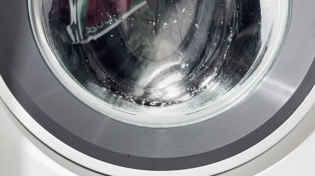 The washing machine runs an active cycle with the drum rotating continuously, water and detergent