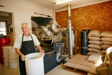 Bucket, equipment and man in coffee roastery for small business, inventory and industry. Happy, entrepreneur and elderly male owner with caffeine beans and machine for production in workshop.