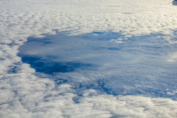 Aerial view above dense clouds with irregular opening revealing blue sky