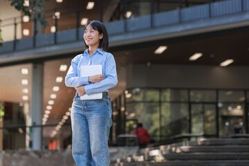 Young asian woman student standing outdoors holding laptop