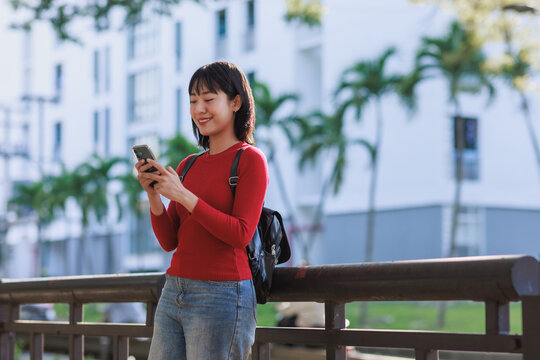 Young asian woman smiling using smartphone outdoors - Powered by Adobe