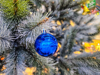 Close-up of a shiny blue Christmas ornament hanging on a frosted artificial pine tree branch.