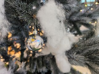 Close-up of a festive Christmas tree decorated with a shiny silver bauble and white fluffy snow.