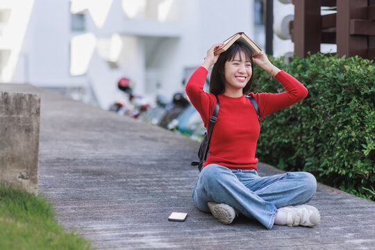 Young student learning outdoors, holding book overhead happily