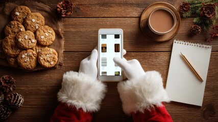 Santa checks his list on a phone while cookies sit on the table
