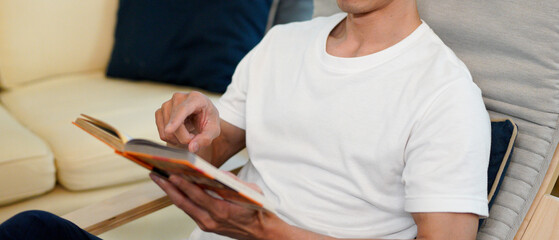 man relaxing at the armchair at home while reading his favorite book