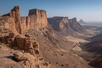 Fototapeta premium The vast, dramatic landscapes of the Hadramawt region, with abstract ancient mud-brick skyscrapers and deep wadis under a clear sky.