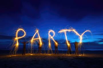 Sparklers light up night as friends gather on beach for joyful party celebration under deep blue sky creating festive and energetic atmosphere
