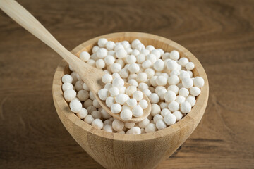 Organic tapioca pearls in wooden bamboo bowl on table closeup. Spoon scooping white dry tapioca pearls, cooking ingredient, gluten free food, healthy eating.