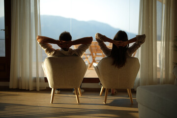 Back view of a couple relaxing at home looking through a window