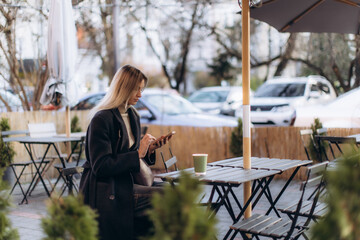Woman scrolling smartphone sitting at outdoor cafe table