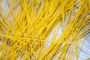 Dry uncooked spaghetti scattered on a wooden surface. Close-up view of raw pasta texture, ideal for cooking, food background or culinary concept.