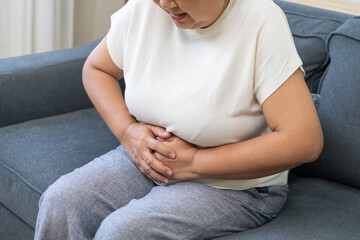 Sick asian senior woman in pain, hand holding belly, stomach pain from food poisoning, older hurt...