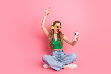 Happy young woman listening to music and taking selfie with phone against a pink background