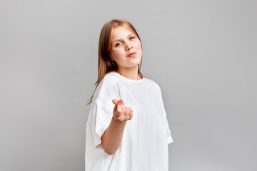 Girl posing in bright studio, making trendy finger heart gesture, love and positivity. Soft lighting, clean neutral background, modern youth culture vibe, playful expression