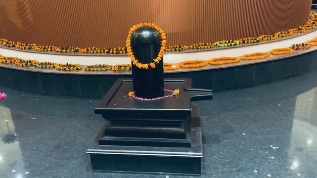 Shiva Lingam installed on a pedestal, surrounded by ritual decorations. The black stone structure symbolizes infinite energy, purity, and the formless aspect of Shiva.