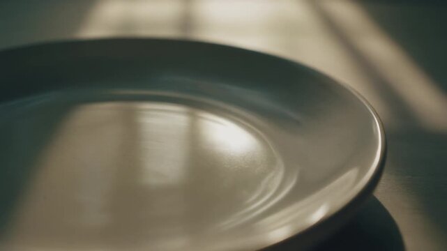 Close-up of an empty, reflective metallic or ceramic plate with soft light and shadow play on its surface.