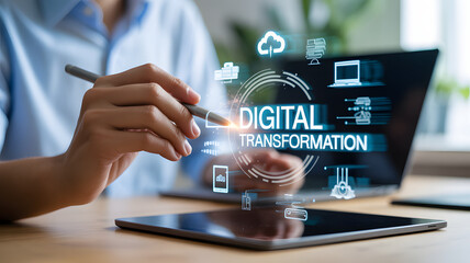 Business person using stylus on tablet interacting with digital transformation concept icons and laptop in background, technology and innovation in modern office setting