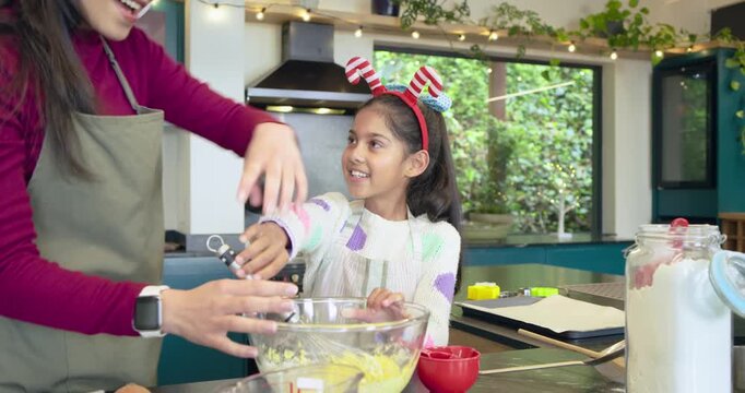 Asian mother guiding daughter mixing yellow batter in bowl on kitchen island for holiday baking