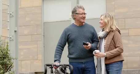 Senior couple greeting, showing smartphone to share info and holding coffee cup by bike on sidewalk - Powered by Adobe