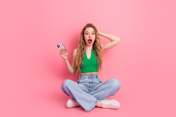Surprised young female holding a smartphone on a pink background, representing modern lifestyle, fashion, and digital connectivity
