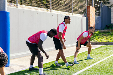 Male soccer players warming up and stretching on an outdoor artificial turf field, preparing for football practice