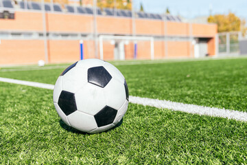 Fototapeta premium Classic black and white soccer ball laying on green synthetic turf, with a white line and blurred goal in background