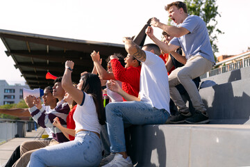 Diverse young people in stadium stands cheering loud, raising fists and clapping hands, celebrating event with excitement