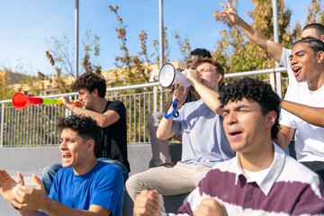 Fototapeta premium Diverse group of male fans watching a sport event from the stadium stands, celebrating and making noise together