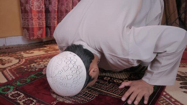 Asian muslim man wearing traditional cap praying in a prostrate position on a prayer mat during Ramadan