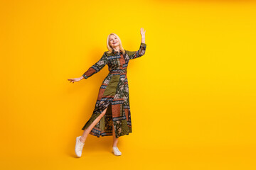 Glamorous mature woman in patchwork dress dances joyfully against a bright yellow background