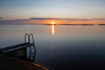 Fototapeta premium Beautiful summer evening with a spectacular sunset over the Gothenburg Archipelago and the calm water of the North Sea seen from the rocky coastline of the small island Vrango with a swimming jetty