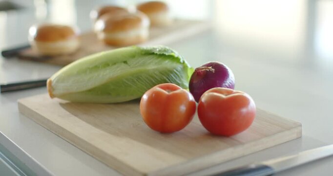 Camera lens shifting focus from tomatoes lettuce and onion to buns highlighting background pastries