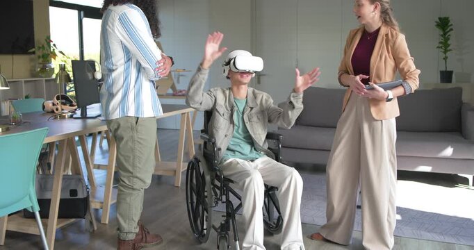 Diverse coworkers inviting man in wheelchair, trying VR headset in office, guiding and high fiving