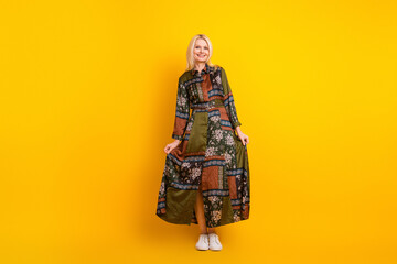 Elegant mature woman in a patchwork dress stands against a bright yellow background smiling and posing for a casual fashion lifestyle stock photo