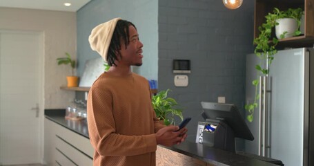 African American customer tapping smartphone at counter paying for coffee and barista handing cup - Powered by Adobe
