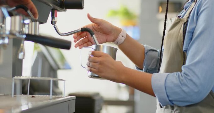 African American woman barista twisting knob, frothing milk in pitcher at cafe counter, copy space