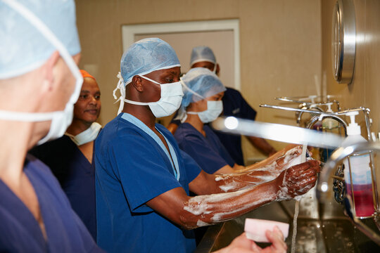 Surgeon, people and washing hands in hospital with soap for medical procedure, disinfection and hygiene. PPE, healthcare workers and masks with water for cleaning, surgical scrub and preparation. - Powered by Adobe