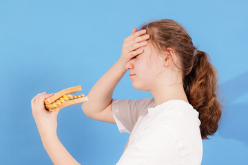 Girl looks frustrated while holding a sandwich against a blue backdrop during lunch time