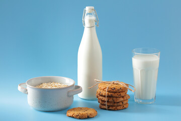 Homemade oatmeal cookies with milk bottle, glass, and bowl of oats on blue background.